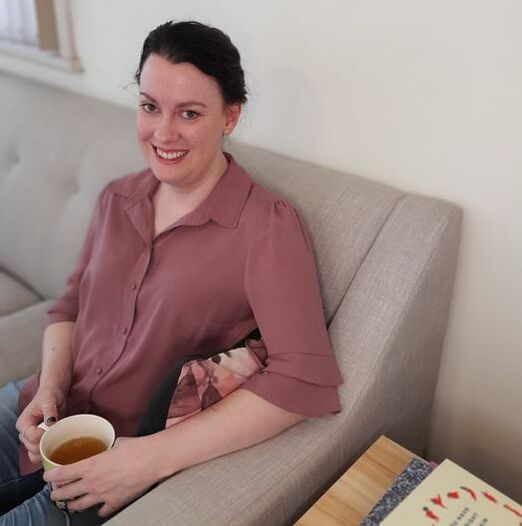 Melissa O'Loughlan is an eating disorder dietitian from Ballarat providing online appointments in Australia.  She is sitting on a grey couch with a cup of tea and smiling at the camera.